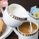 A person pouring milk into a cup of coffee using a Syracuse China Baroque bone china creamer.