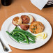 A Libbey ivory porcelain pellet plate with green beans, potatoes, and meat on a table.