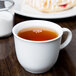 A Libbey Reflections white porcelain tea cup filled with tea on a table.