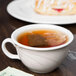 A Libbey ivory flint porcelain low tea cup filled with tea on a table with a pastry.