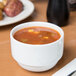 A white Libbey porcelain bouillon cup filled with soup on a table.