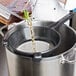 A chef using a Matfer Bourgeat Exoglass strainer to pour liquid into a pot.