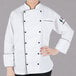 A woman wearing a Mercer Culinary white chef jacket with black piping.