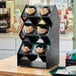 A black Vollrath countertop flatware organizer with black cylinders holding spoons and forks.