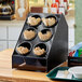 A black Vollrath countertop organizer with black and white flatware cylinders holding spoons and forks.