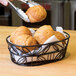An American Metalcraft wrought iron oval basket with a leaf design holding rolls.