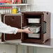 A woman opening a dark brown front-loading Cambro food pan carrier.