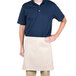 A man wearing a blue shirt and ivory waist apron standing at a counter in a professional kitchen.