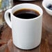 A close-up of a 10 Strawberry Street Royal White porcelain c-handle mug filled with brown liquid.