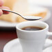 A hand holding a Libbey stainless steel demitasse spoon over a cup of coffee.