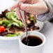 A hand holding a Libbey stainless steel teaspoon over a cup of liquid.