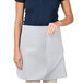 A woman wearing a gray Intedge waist apron over a blue shirt.