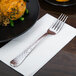 A Libbey stainless steel dinner fork on a napkin next to a plate of food.