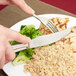 A person using a Libbey stainless steel dinner knife to cut a piece of broccoli on a plate of food.