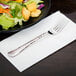 A Libbey stainless steel extra heavy weight utility fork on a napkin next to a plate of salad.