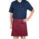 A man wearing a burgundy apron with tan pants on a counter in a professional kitchen.