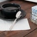 A cup of tea on a saucer with a Libbey stainless steel demitasse spoon.