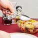 A hand holding a Libbey stainless steel serving spoon over a bowl of food.