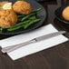 A Libbey stainless steel dinner knife on a white napkin next to a plate of food on a table.