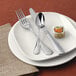 A plate with silverware including a Reserve by Libbey Baroque stainless steel demitasse spoon.