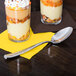 A Libbey stainless steel dessert spoon on a napkin next to two glasses of dessert with whipped cream and sprinkles.