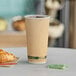 A close-up of an EcoChoice Double Wall Kraft paper hot cup full of coffee on a table with a croissant.