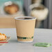 A close-up of an EcoChoice Double Wall Kraft Paper Hot Cup full of coffee on a table with a croissant.