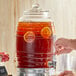 A person pouring iced tea into an Acopa glass beverage dispenser.