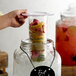 A hand holding a round Acopa glass jar filled with fruit on a table.