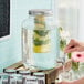 A hand pouring water from a faucet into a glass jar with lemons and vegetables inside.