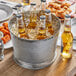 A Choice metal bucket filled with beer bottles on a table on an outdoor patio.