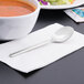 A Libbey stainless steel bouillon spoon on a napkin next to a bowl of soup.