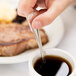 A person holding a Libbey Geneva European teaspoon over a cup of coffee.