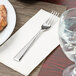 A Libbey stainless steel salad fork on a napkin next to a plate of food.