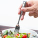 A hand holding a Libbey stainless steel salad fork over a bowl of salad.