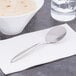 A Libbey stainless steel bouillon spoon on a napkin next to a bowl of soup.