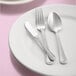 A white plate with silverware, including a Libbey stainless steel serving spoon, on it.