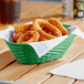 A Carlisle green oval plastic serving basket filled with fried onion rings on a table on an outdoor patio.