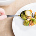 A hand holding a Libbey stainless steel serving spoon over a plate of brussels sprouts and nuts.