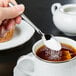 A person holding a Libbey stainless steel demitasse spoon with sugar over a cup of tea.