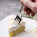 A hand using a Libbey stainless steel dessert fork to cut a piece of cake.