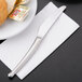 A World Tableware stainless steel bread and butter knife on a table with a plate of bread and butter.