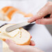 A person using a Libbey stainless steel butter spreader to spread butter on a piece of bread.