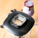 A Waring blender with a black lid on a counter with a glass of purple liquid.