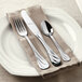 A white plate with a Libbey stainless steel bouillon spoon on a napkin with a fork.