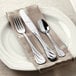 A white plate with Libbey stainless steel dinner knife and fork on a napkin.