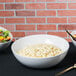 A white Tablecraft Sierra melamine bowl filled with macaroni salad on a table with bowls of food.