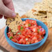 A hand holding a chip and dipping it into a bowl of salsa.