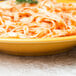 A Libbey porcelain pasta bowl filled with saffron pasta and tomato sauce on a table.