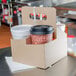 A Sabert drink carrier holding four coffee cups with lids in a cardboard box on a table.